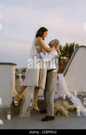 Seitenansicht des Bräutigams, der die Braut in Armen hält, während er auf dem Dach steht Stockfoto