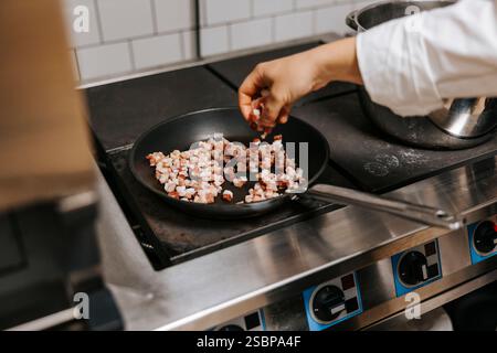 Weibliche Köchin kocht in der Küche des Restaurants Fleisch in der Pfanne auf dem Herd Stockfoto