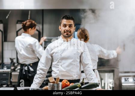 Porträt eines lächelnden jungen männlichen Küchenchefs, der in Uniform in der Restaurantküche steht Stockfoto