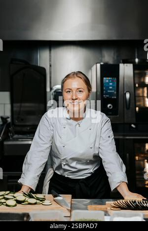 Porträt einer lächelnden Küchenchefin in weißer Uniform und auf der Theke in der Küche im Restaurant Stockfoto