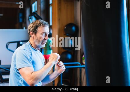 Ein Mann schlägt eine Tasche in einem Fitnessstudio. Der Mann trägt ein blaues Hemd und ist gut gelaunt Stockfoto