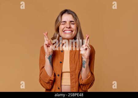 Eine fröhliche junge Frau lächelt breit und drückt ihre Finger in der Hoffnung auf Glück. Ihr stylisches Outfit bildet einen schönen Kontrast zu der warmen, sonnigen Ba Stockfoto