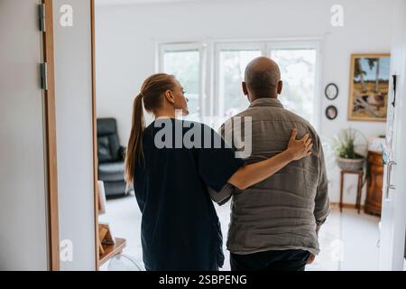 Rückansicht einer Hausmeisterin beim Gehen mit Seniorenmännchen im Pflegeheim Stockfoto