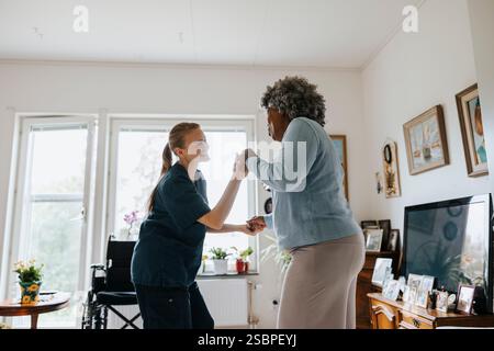 Glückliche Krankenschwester tanzt mit Seniorin im Pflegeheim Stockfoto