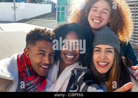 Vier fröhliche, multiethnische junge Studenten lächeln zusammen im Freien, genießen ihre Zeit in der Wintersonne und feiern Freundschaft und Einheit Stockfoto