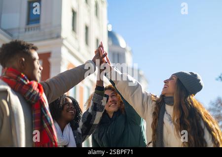 Vier fröhliche Studenten schließen sich zusammen und feiern ihre Teamarbeit und Zusammenarbeit vor ihrer Universität Stockfoto