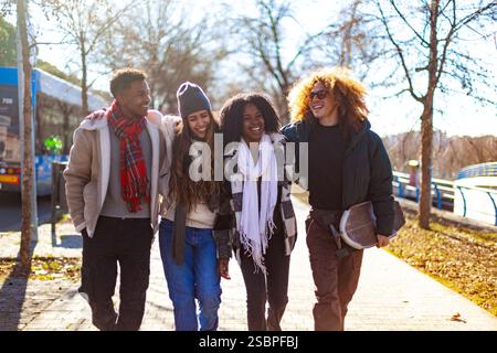 Vier fröhliche, multiethnische Studenten gehen an einem sonnigen Wintertag zusammen Stockfoto