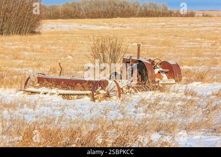 Ein alter Traktor sitzt im Schnee auf einem Feld. Der Traktor ist rostig und hat einen schwarzen Motor Stockfoto