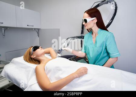 Ein erfahrener Arzt führt die Laserhaarentfernung an einem Patienten in einer schlanken klinischen Umgebung durch. Stockfoto