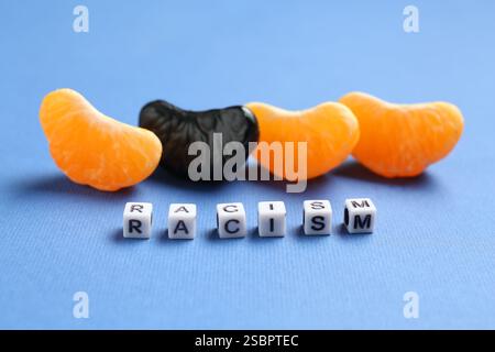 Wort Rassismus und Mandarinensegmente in verschiedenen Farben auf blauem Hintergrund, Nahaufnahme Stockfoto
