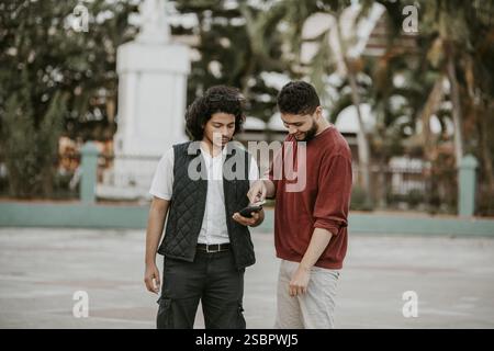 Porträt von zwei lächelnden Kerlen, die draußen ein Handy benutzen. Zwei glückliche Freunde, die das Handy auf der Straße benutzen Stockfoto