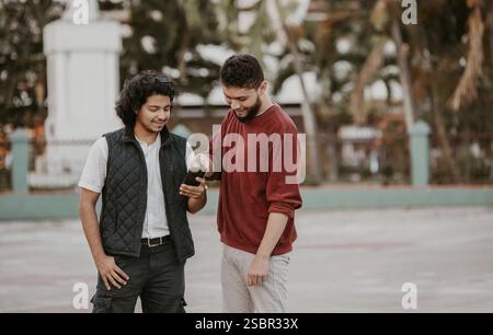 Zwei glückliche Freunde, die das Handy auf der Straße benutzen. Porträt von zwei lächelnden Kerlen, die draußen ein Handy benutzen Stockfoto