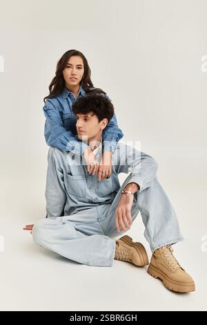 Selbstbewusstes junges Paar in passenden Denim-Outfits posiert stilvoll vor einem neutralen Hintergrund. Stockfoto