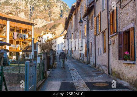 Ein älterer Mann geht mit seinem Hund in einer ruhigen Gasse im historischen Dorf Andreis. Provinz Pordenone, Friaul-Julisch Venetien, Nordost-Italien. Stockfoto
