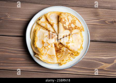 Hausgemachte Crepes-Pfannkuchen auf Teller und hölzernem Hintergrund, Blick von oben. Stapel französischer Crepe Suzette. Traditionelles russisches Blini zum Maslenitsa-Frühstück. Stockfoto