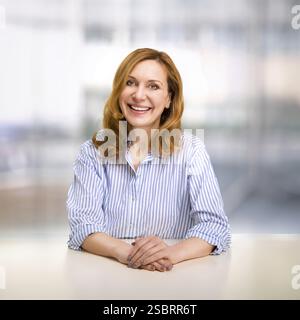 Lächelnde, selbstbewusste, stilvolle, reife Frau mittleren Alters im Büro. Leitende Geschäftsfrau, leitende Geschäftsführerin, die Kameraarme überkreuzt betrachtet, Stockfoto