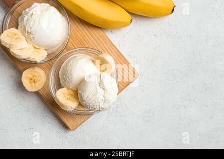 Eiskugeln und Bananenscheiben in Schüsseln auf weißem Tisch, Blick von oben, Kopierraum. Gesundes rohes veganes Bananeneis (Nicecream), hausgemachte Bio-des Stockfoto