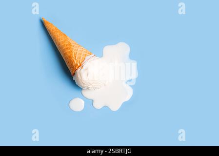 Weißes Eis schmilzt und verschüttet von der Waffelkegel auf pastellblauem Hintergrund. Minimales, trendiges, kreatives Konzept für Sommergerichte. Geschmolzene Schaufel Stockfoto
