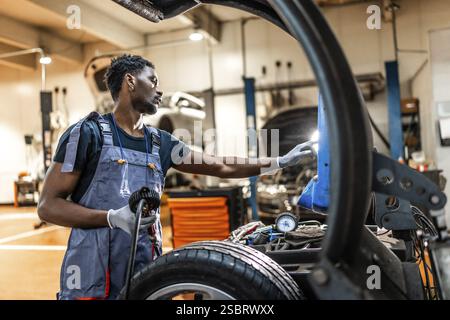 Junger Mechaniker, der an der Fahrzeugwartung arbeitet, Räder und Fahrgestell in einer professionellen Autowerkstatt überprüft Stockfoto