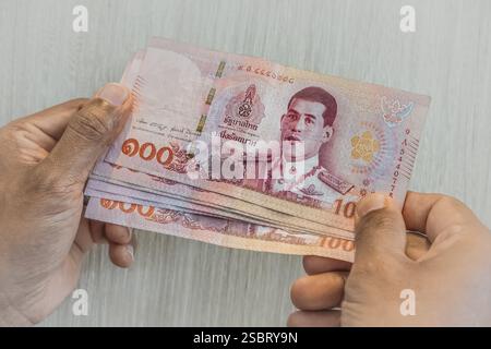 Mann, der Thai Baht in den Händen hält. Thailändische Baht-Banknoten Bargeld. Thailand Banknote 1000 Baht Papiergeld auf hellem Hintergrund. Handhaltung in der Nähe Stockfoto