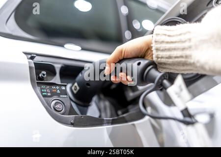 Nahaufnahme einer Hand, die in einem Autohändler ein Ladekabel in ein Elektrofahrzeug einsteckt, um den Übergang zu nachhaltigem Transport zu demonstrieren Stockfoto