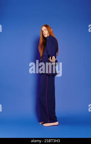 Ein hübscher junger Mann mit langen roten Haaren schlägt eine modische Pose auf einem hellblauen Hintergrund. Stockfoto