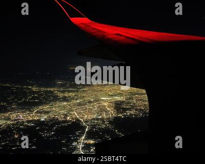 Aus der Vogelperspektive auf die Stadt und glitzernde Lichter bei Nacht vom Flugzeugfenster Stockfoto