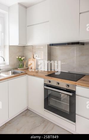 Eine Kücheneinrichtung mit Holzarbeitsfläche und Herd. Ablagefläche in moderner weißer Küche. Stilvolle Küche Waschbecken mit Holzschränken und Bla Stockfoto