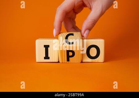 ICO vs. IPO-Symbol. Geschäftsmann Hand dreht Holzwürfel und ändert das Wort IPO in ICO. Wunderschöner orangefarbener Hintergrund. ICO vs IPO und Geschäftskonzept. Stockfoto