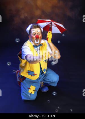 Ein lustiger Clown mit lächelndem, fröhlichem Ausdruck, auf farbigem Hintergrund Stockfoto
