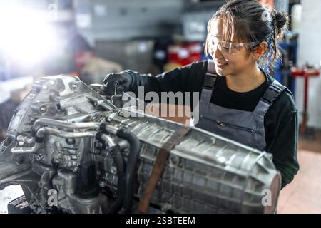 Asiatische Mechanikerin arbeitet fleißig an einem Fahrzeuggetriebe in einer professionellen Garage und zeigt Können und Know-how in der Autoreparatur Stockfoto