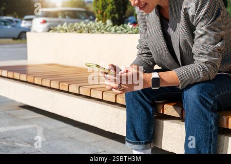 Moderne Frau, die auf der Stadtbank sitzt und Nachrichten auf dem Smartphone sendet Stockfoto