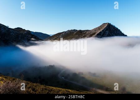 Misty Mountain Valley Road Scene, eine gewundene Straße schlängelt sich durch den Talboden mit Bergen, die auf beiden Seiten aufsteigen, teilweise von einem dicken L verdeckt Stockfoto