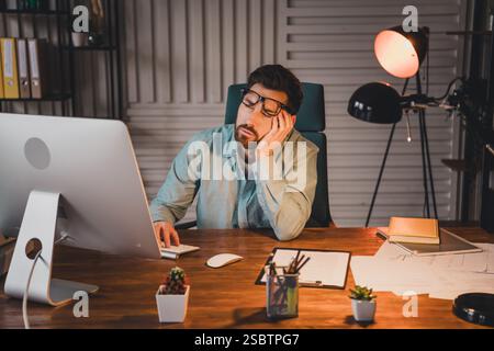 Müder junger Mann, der sich am Schreibtisch im Büroarbeitsbereich ausruhen lässt Stockfoto