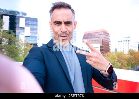 Selbstbewusster Mann, der ein Selfie macht und das Friedenszeichen Outdoorsc zeigt Stockfoto