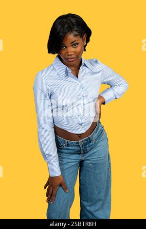Studio-Porträt einer stilvollen jungen schwarzen Frau, die selbstbewusst vor einem leuchtend gelben Hintergrund posiert Stockfoto