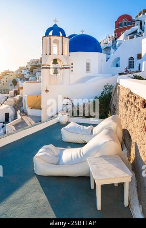 Zwei Sonnenliegen in der Abendsonne vor der Kirche St. Spyridon mit den blauen Kuppeln in Oia, Kykladen, Griechenland Stockfoto