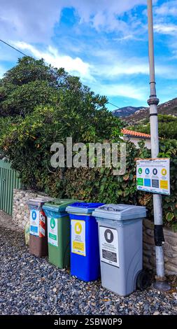 Vier bunte Müllcontainer am Strand vor dem Hintergrund grüner Sträucher und blauer Himmel. Umweltschutz. Denken Sie anders Stockfoto