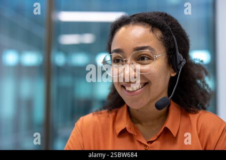 Junge, erfolgreiche Supportmitarbeiter am Arbeitsplatz im Büro mit Headset, Frau, die aus der Nähe lächelt und zur Seite blickt. Stockfoto