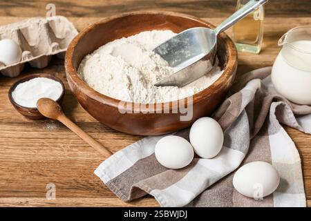 Frische Eier, eine Schüssel Mehl, Öl, Backpulver und Milch auf Holztisch Stockfoto