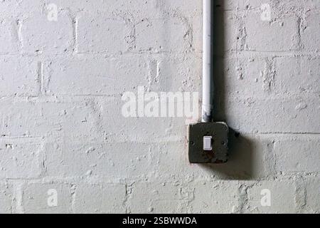 Einsamer industrieller Lichtschalter an weiß lackierter Ziegelwand mit Textur Stockfoto