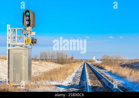 Das Bahnübergangsschild ist an einem Pfosten. Das Schild ist grün und sagt „R“. Das Schild ist auf einem verschneiten Feld Stockfoto
