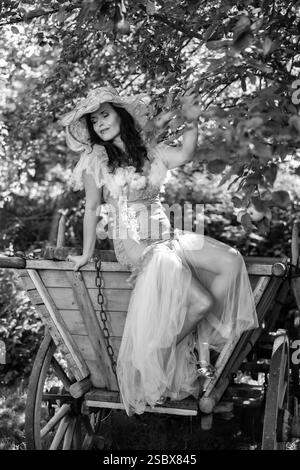 Eine reife Frau über 50 auf einem Holzwagen an einem alten Apfelbaum in einem verwunschenen Garten / Eine reife Frau über 50 auf einem Holzwagen von einem alten Stockfoto