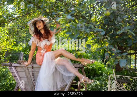 Eine reife Frau über 50 auf einem Holzwagen an einem alten Apfelbaum in einem verwunschenen Garten / Eine reife Frau über 50 auf einem Holzwagen von einem alten Stockfoto