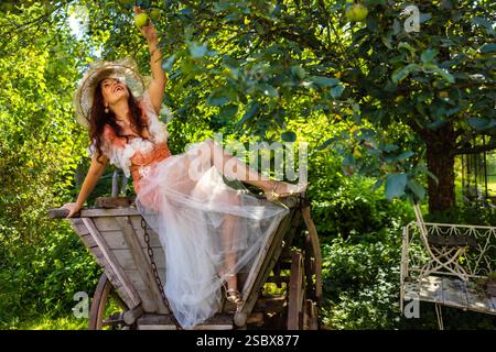Eine reife Frau über 50 auf einem Holzwagen an einem alten Apfelbaum in einem verwunschenen Garten / Eine reife Frau über 50 auf einem Holzwagen von einem alten Stockfoto