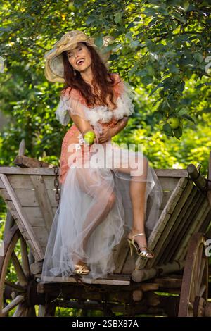 Eine reife Frau über 50 auf einem Holzwagen an einem alten Apfelbaum in einem verwunschenen Garten / Eine reife Frau über 50 auf einem Holzwagen von einem alten Stockfoto