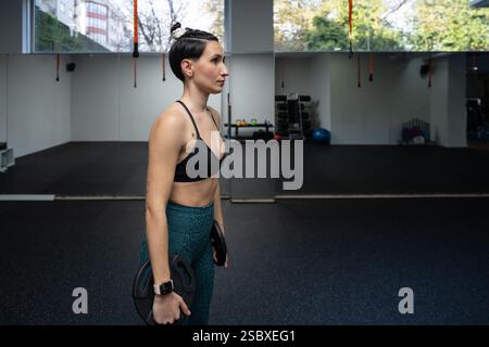 Die junge athletische Frau hält Gewichte im Fitnessstudio und bereitet sich auf ein intensives Workout vor, das sich auf den Kraftaufbau und die Verbesserung der Fitness konzentriert Stockfoto
