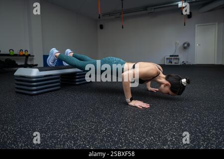 Athletische Frau, die erhöhte Liegestütze macht, die Kernkraft anspricht, während sie intensiv in einem eleganten Fitnessstudio trainiert, was ihr Engagement für das persönliche zeigt Stockfoto