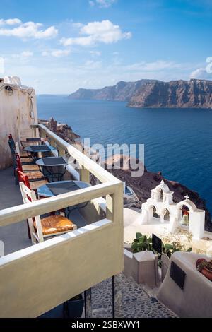 Farbenfrohe Holzstühle und Metalltische auf dem Balkon eines Cafés in Oia mit Blick auf die Caldera von Santorin, Ägäis, Griechenland Stockfoto