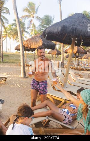 Ein mittelalter Tourist serviert einer entspannten Frau ein Glas Bier im Strandresort Grand Palladium Imbassai, Salvador de Bahia, Brasilien Stockfoto